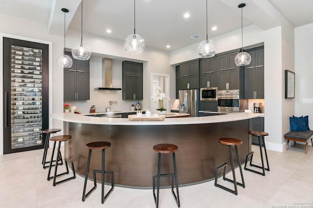 kitchen with wall chimney exhaust hood, appliances with stainless steel finishes, light countertops, and a breakfast bar area