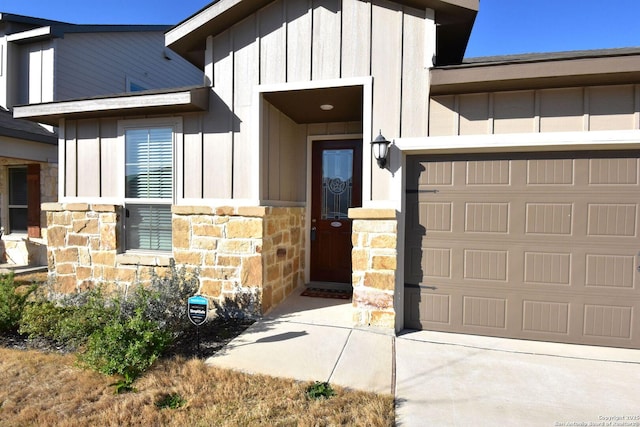 view of exterior entry featuring driveway, stone siding, a garage, and board and batten siding