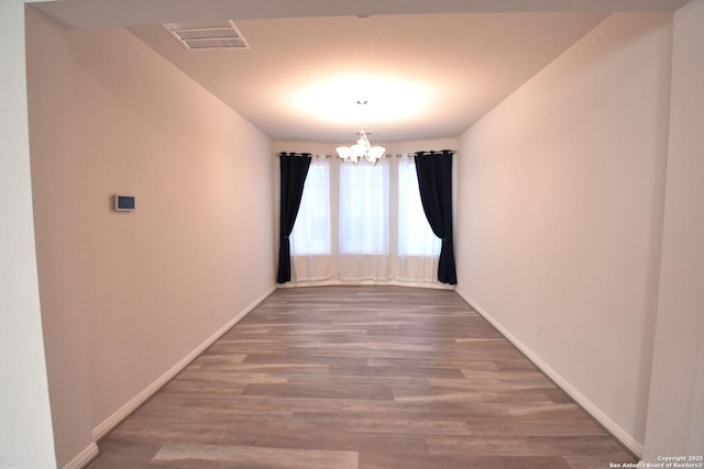 empty room featuring wood finished floors, visible vents, baseboards, and an inviting chandelier