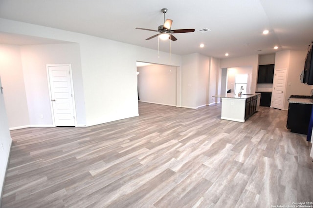 unfurnished living room featuring light wood-style flooring, a sink, visible vents, and a ceiling fan