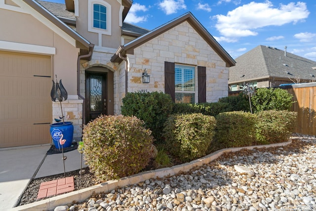 entrance to property featuring a garage, stone siding, a shingled roof, and stucco siding