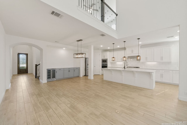 unfurnished living room with light wood finished floors, wine cooler, a sink, and visible vents