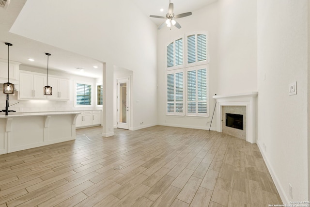 unfurnished living room with baseboards, a towering ceiling, ceiling fan, light wood-style floors, and a fireplace