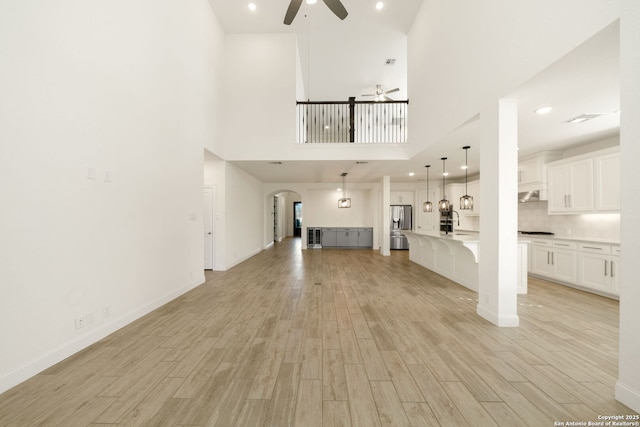 unfurnished living room with ceiling fan, arched walkways, light wood-style flooring, and baseboards