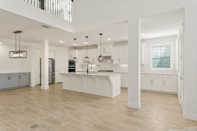 kitchen with stainless steel appliances, light countertops, light wood-style flooring, a sink, and a kitchen bar