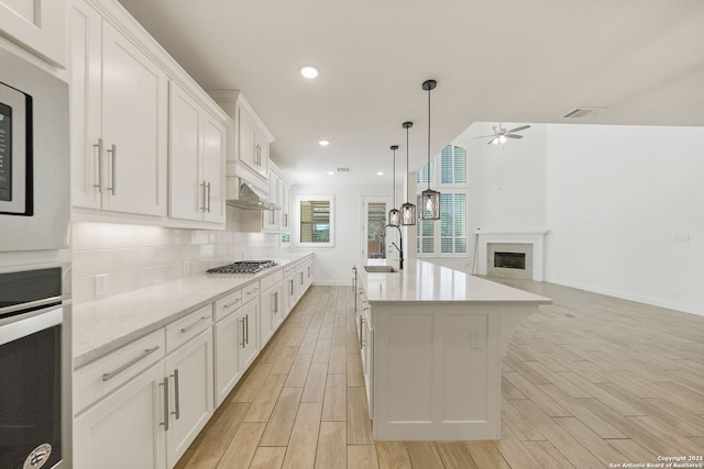 kitchen featuring oven, wood tiled floor, stainless steel gas stovetop, a fireplace, and backsplash