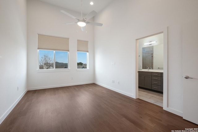 unfurnished bedroom featuring dark wood finished floors, a high ceiling, connected bathroom, a sink, and baseboards