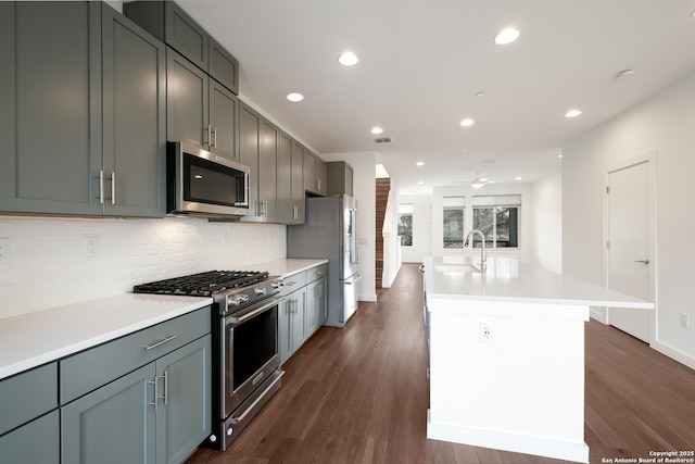 kitchen with stainless steel appliances, dark wood-type flooring, a sink, light countertops, and backsplash