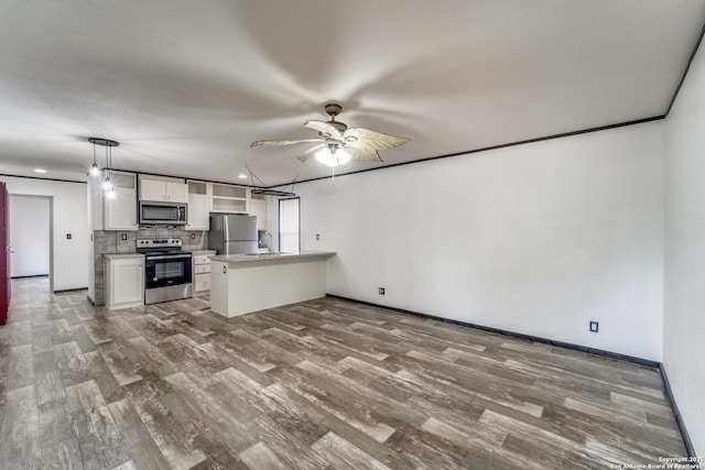 kitchen with stainless steel appliances, a peninsula, wood finished floors, a sink, and white cabinetry