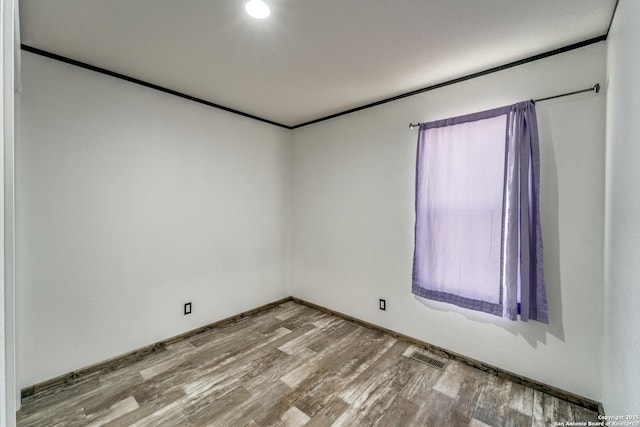 spare room featuring wood finished floors, visible vents, a healthy amount of sunlight, baseboards, and ornamental molding