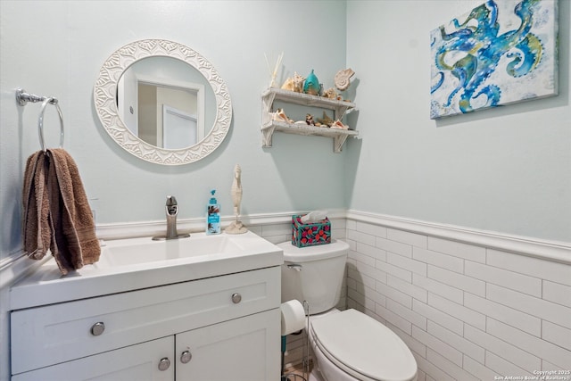 half bath with tile walls, wainscoting, vanity, and toilet