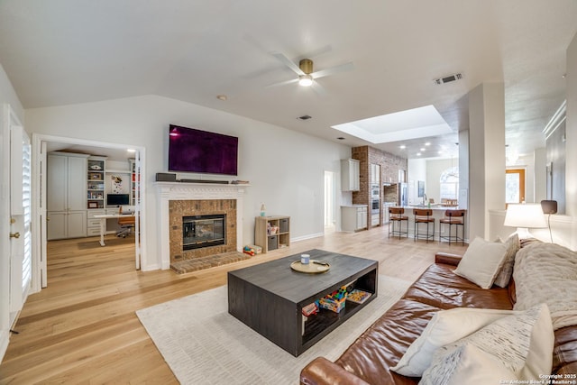 living room with lofted ceiling, light wood-type flooring, a glass covered fireplace, and visible vents