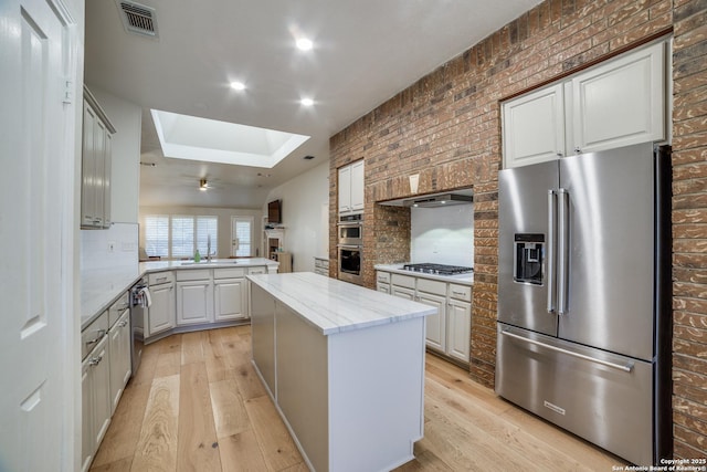 kitchen with appliances with stainless steel finishes, a skylight, light wood-style floors, and a kitchen island