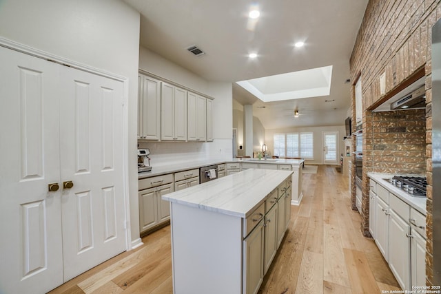 kitchen with a skylight, a center island, visible vents, light wood-style floors, and a peninsula