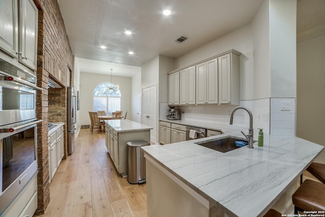 kitchen with a center island, tasteful backsplash, visible vents, a sink, and light wood-type flooring