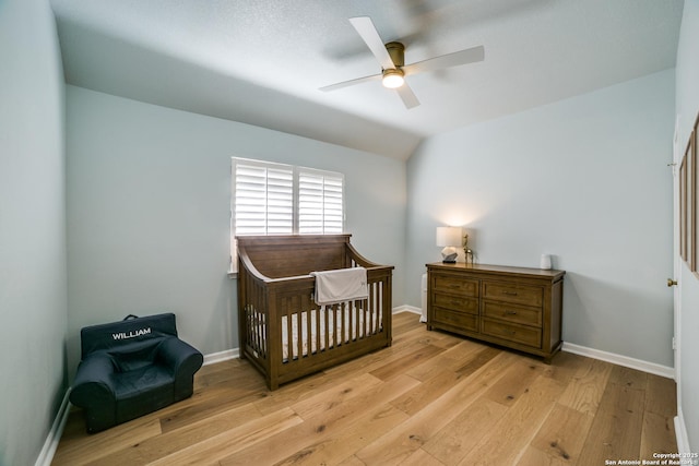 bedroom with lofted ceiling, a nursery area, light wood-style flooring, and baseboards