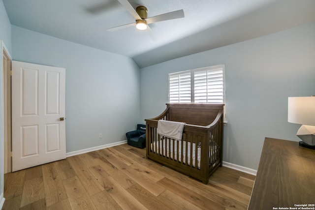 bedroom with a crib, baseboards, vaulted ceiling, and hardwood / wood-style floors