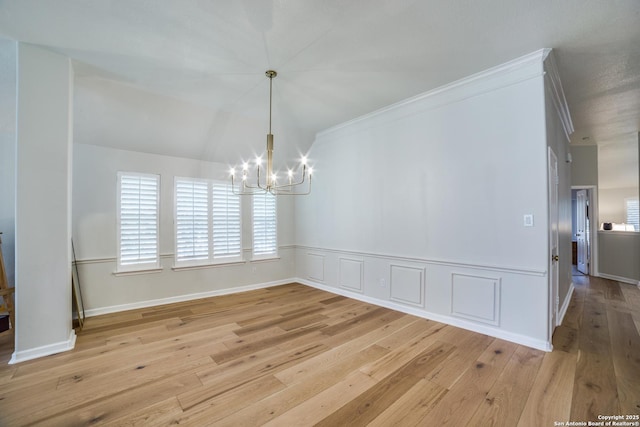 unfurnished dining area with ornamental molding, a decorative wall, light wood-style flooring, and an inviting chandelier