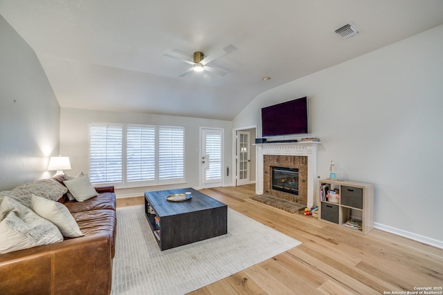 living room featuring visible vents, a ceiling fan, a tile fireplace, wood finished floors, and vaulted ceiling