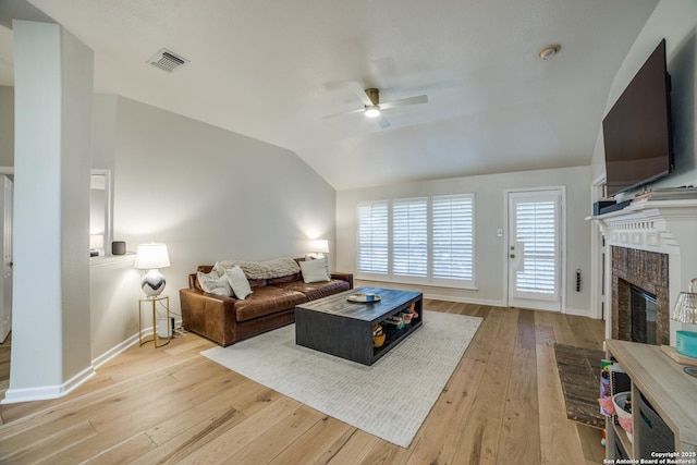 living room featuring lofted ceiling, a ceiling fan, visible vents, light wood-style floors, and a brick fireplace