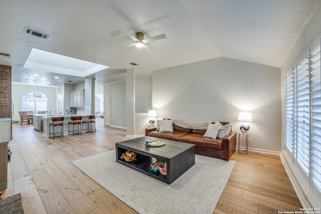 living room featuring light wood-style flooring, visible vents, vaulted ceiling, and a ceiling fan