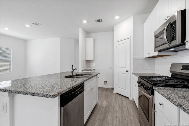 kitchen featuring appliances with stainless steel finishes, dark stone counters, visible vents, and a sink