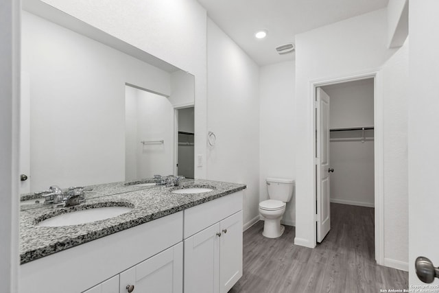 bathroom with toilet, a walk in closet, a sink, and wood finished floors