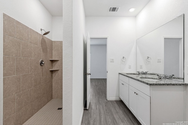 full bathroom with a sink, wood finished floors, visible vents, a tile shower, and double vanity