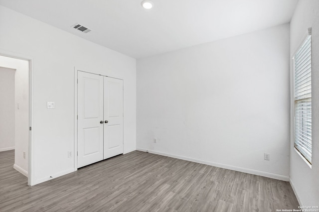 unfurnished bedroom with a closet, visible vents, baseboards, and wood finished floors