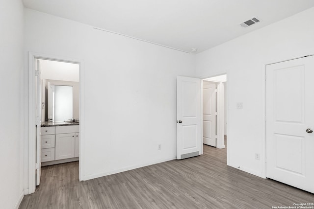 unfurnished bedroom featuring visible vents, ensuite bath, light wood-style flooring, and baseboards