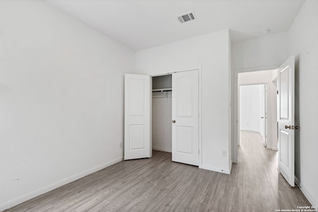 unfurnished bedroom featuring baseboards, a closet, visible vents, and wood finished floors