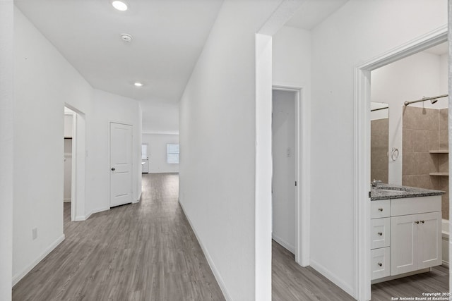 corridor with baseboards, recessed lighting, a sink, and light wood-style floors