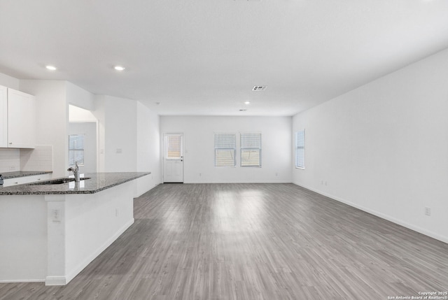 kitchen featuring baseboards, white cabinets, light wood-style flooring, open floor plan, and dark stone countertops