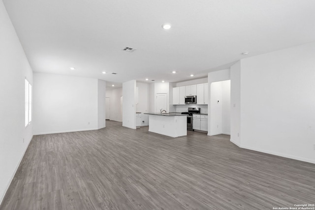 unfurnished living room with baseboards, wood finished floors, visible vents, and recessed lighting