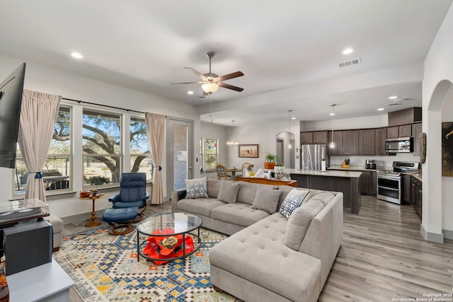 living room featuring arched walkways, visible vents, light wood finished floors, and recessed lighting