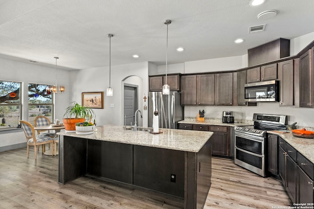 kitchen featuring light wood finished floors, visible vents, light stone countertops, stainless steel appliances, and dark brown cabinets