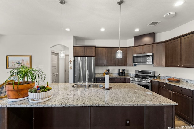 kitchen with appliances with stainless steel finishes, a sink, dark brown cabinetry, and decorative light fixtures