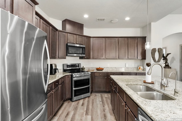 kitchen featuring light wood-style flooring, dark brown cabinetry, stainless steel appliances, a sink, and visible vents