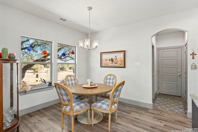 dining room with arched walkways, baseboards, visible vents, and light wood finished floors