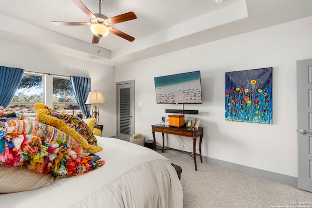 carpeted bedroom with ceiling fan, baseboards, and a raised ceiling