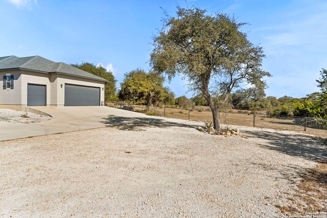 view of yard featuring a garage, concrete driveway, and fence