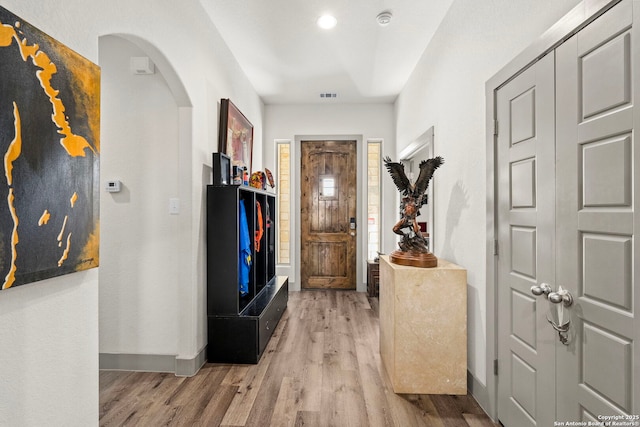 foyer entrance with arched walkways, light wood-type flooring, visible vents, and baseboards