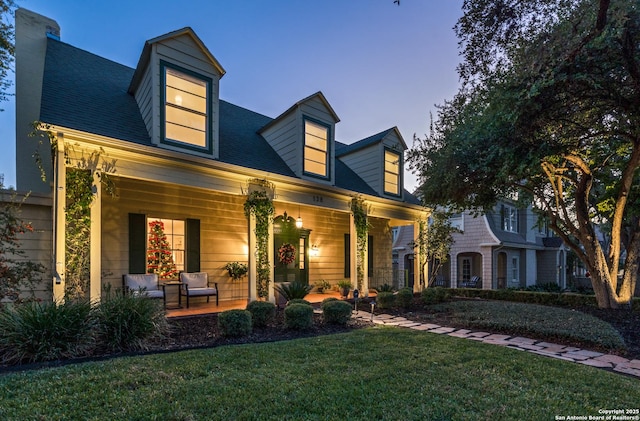 new england style home featuring covered porch and a yard