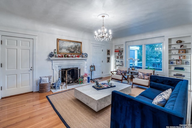 living area with an inviting chandelier, built in shelves, a fireplace with raised hearth, and wood finished floors