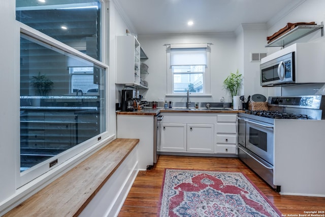 kitchen with visible vents, white cabinets, wood finished floors, stainless steel appliances, and crown molding