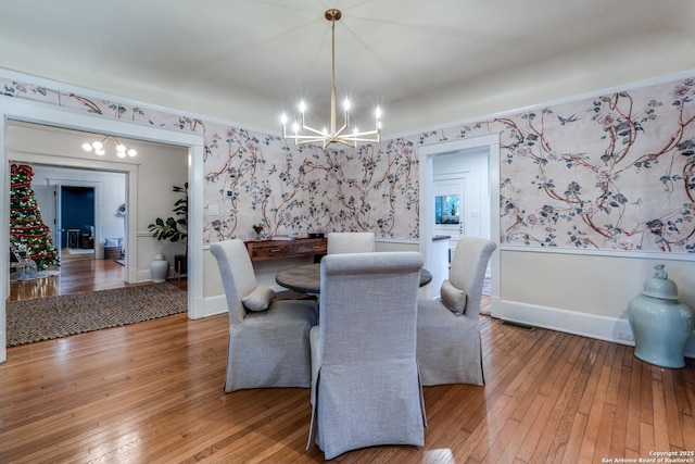 dining room featuring a chandelier, light wood-style floors, baseboards, and wallpapered walls