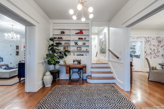 stairs with wallpapered walls, built in shelves, a notable chandelier, and wood finished floors