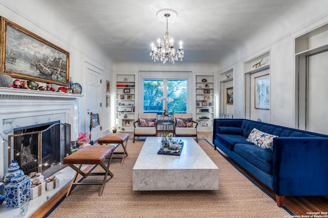 living area with built in features, a fireplace with raised hearth, a notable chandelier, and wood finished floors