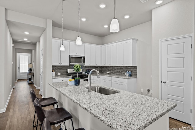 kitchen with dark wood-type flooring, a sink, range with gas stovetop, decorative backsplash, and stainless steel microwave