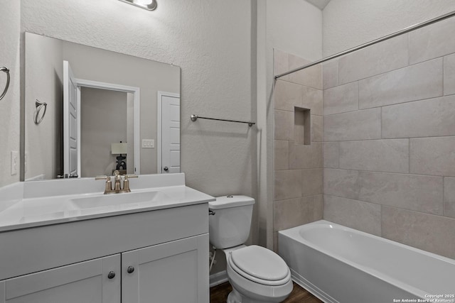 full bath with a textured wall, toilet, wood finished floors, bathing tub / shower combination, and vanity